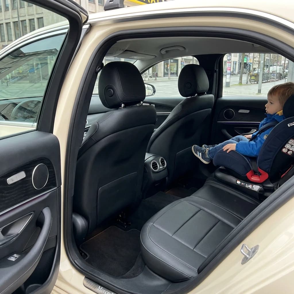 Blick durch die offene Tür auf den Rücksitz eines Taxis, ein Kind sitzt im Kindersitz